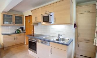 A modern kitchen with bright furniture and a refrigerator. The equipment includes a stove, a microwave, and a sink.