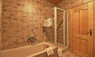 A modern bathroom with a bathtub and a shower. The walls are tiled and a wooden terrace door leads outside.