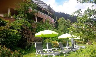 A beautiful garden with loungers and sun umbrellas. In the background, a building and a lot of greenery can be seen.