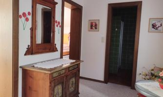 A hallway with a wooden sideboard and a mirror. Decorative flowers are on the wall and two doors lead to other rooms.
