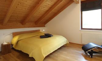 A cozy bedroom with a large bed and a yellow duvet. The room features wooden ceilings and a window with a view to the outside.