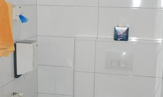 A bright bathroom with white tiles. There is a toilet, a hairdryer, and a towel.