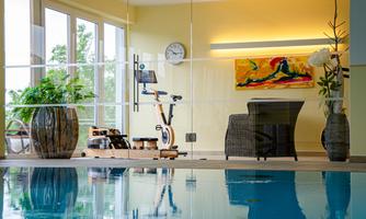 A modern gym with a view of a pool. Plants and a piece of art create a relaxed atmosphere.