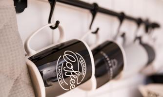 Three elegant coffee cups hang on a black rod in a modern kitchen. The cups have an appealing label and give the room a cozy character.