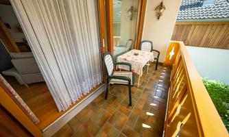A cozy balcony with a table and two chairs. The sun shines through the curtains and the floor is tiled.
