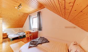 A cozy bedroom with a wooden ceiling and two single beds. A window with curtains allows natural light in.