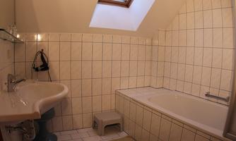 A simple bathroom with a bathtub and a sink. It has bright tiles and a skylight.