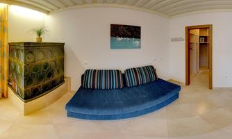 A modern living room with a blue sofa and an artistic wall mural. On the left is a decorative stove and on the right, a door leads to another room.