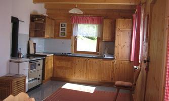 A cozy kitchen with wooden furniture and windows that let in plenty of light. The room has an inviting atmosphere and is functionally furnished.