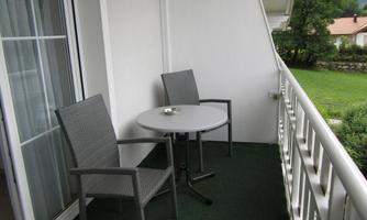 A balcony with two chairs and a small table. The area is designed in green and offers a view of the surroundings.