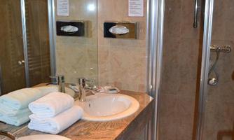A modern bathroom with a double sink and a shower. Soft towels are neatly placed on the shelf.