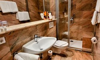 A modern bathroom with a shower, a sink, and toilet paper. The walls are clad in clean, marbled material.