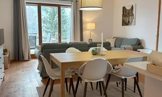 A cozy living room with a large dining table and chairs. A bright window lets in plenty of light, and the room has a modern, inviting atmosphere.