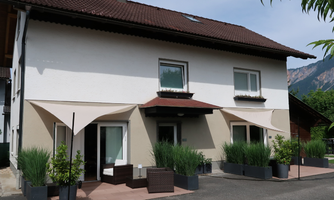 A modern house with a small garden area. Cozy seating and plant pots stand in front of the entrance.