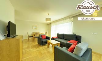A modern living room with a comfortable sofa and a table. Large windows provide plenty of daylight.