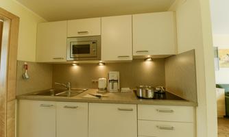 A modern kitchen with bright cabinets and a microwave oven. On the countertop are a coffee machine and cookware.