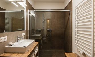 A modern bathroom with a spacious glass shower and an elegant sink. The warm wooden elements and dark tiles create a cozy atmosphere.