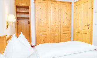 A cozy bedroom with wooden paneling and a large wardrobe. The bed is designed to be simple and inviting.