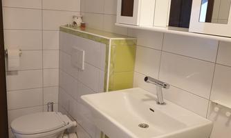 A modern bathroom with white tiles and a sink. The decor is simple and stylish, with green accents.