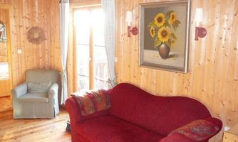 A cozy living room with a red sofa and a comfortable armchair. A painting of sunflowers hangs on the wall, and large windows let in plenty of light.