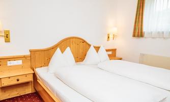 A cozy bedroom with a double bed and two large pillows. The walls are light and the furniture is made of light wood.
