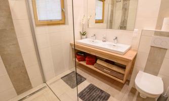 A modern bathroom with a spacious double vanity and a glass shower. The wooden bench provides space for towels and decorative plants.
