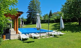 A beautiful pool in a garden with lots of greenery. There are lounge chairs and umbrellas for relaxation.
