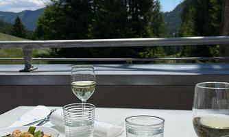 A table outdoors with a beautiful view of trees and the sky. On the table are a delicious vegetable platter and glasses of wine.