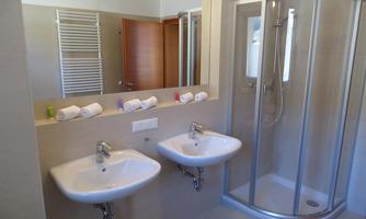 A modern bathroom with two sinks and a shower. The walls are bright and there are fresh towels on the sinks.