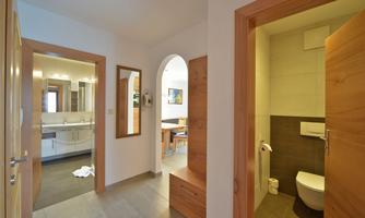 A bright hallway with two doors leading to a bathroom and a living space. The walls are in neutral colors and there are wood details.