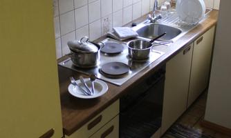 A small, bright kitchen with a wooden workspace and modern kitchen cabinets. Pots and dishes can be seen on the countertop.