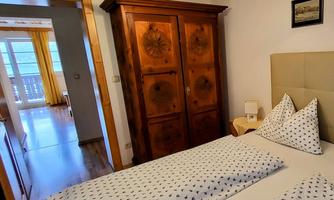 A cozy bedroom with a wooden wardrobe and two beds. The room is bright and inviting, featuring windows and yellow curtains.