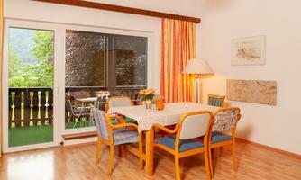 A bright dining room with a table and four chairs. Large windows offer a view of a balcony with a green outlook.