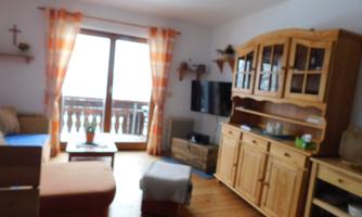 A cozy living room with wooden furniture and large windows. The walls are light and there is a view of the balcony.
