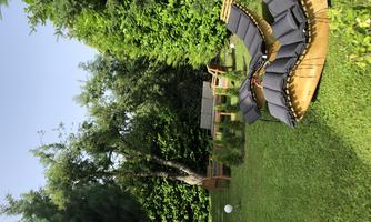 A beautiful garden with a curved wooden lounge and green vegetation. The sky is clear and there are many trees in the background.