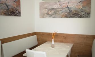 A cozy dining area with a white table and chairs. Decorative pictures hang on the walls, and a lamp hangs over the table.