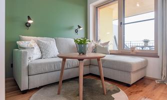 A cozy living area with a bright sofa and a round table. A large window provides light and a view of the terrace.