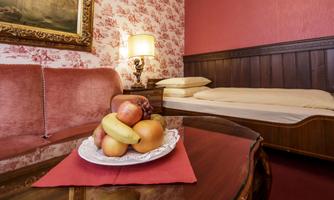 A cozy room with a red sofa and a table with fruit on it. In the background, a bed and a lamp are visible.