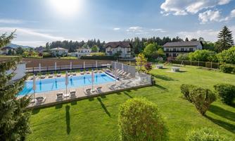 A sunny outdoor area with a swimming pool and loungers. Surrounded by well-kept greenery and trees, the setting offers a relaxed atmosphere.
