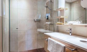 A modern bathroom with an elegant shower and a bright tiled floor. The washing area is equipped with stylish wooden shelves and a large mirror.
