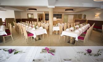 An elegantly decorated event room with long tables and chairs. The tables are adorned with white tablecloths and floral arrangements.