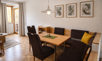 A modern dining room with a wooden table and upholstered chairs. Decorative pictures hang on the wall, and plenty of natural light streams through the windows.