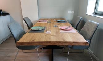A simple dining area with a large wooden table and comfortable chairs. The table is set with colorful dishes and glasses.