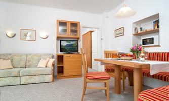 A bright living room with a cozy sofa and a dining area. A television and decorative elements create an inviting atmosphere.