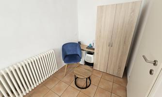 A small room with a blue chair and a table. There is a cupboard against the wall and a radiator is visible.