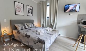 A modern bedroom with a double bed and a TV on the wall. The walls are light and decorated with pictures and an inspiring quote.