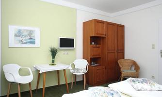 A bright room with two single beds, a table, and chairs.  
On the wall, there is a small television and a wooden wardrobe.