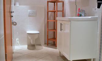 A modern bathroom with bright tiles and a sink. There is a toilet and a wooden shelf for towels.