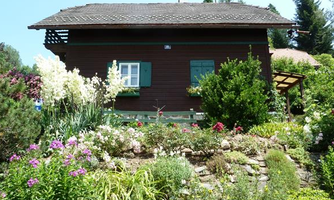A charming wooden house surrounded by a colorful flower garden. Green plants and flowers bloom abundantly in front of the house.
