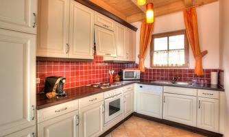 A modern kitchen with white cabinets and red tiles. It is well-equipped with appliances and has large windows for plenty of daylight.